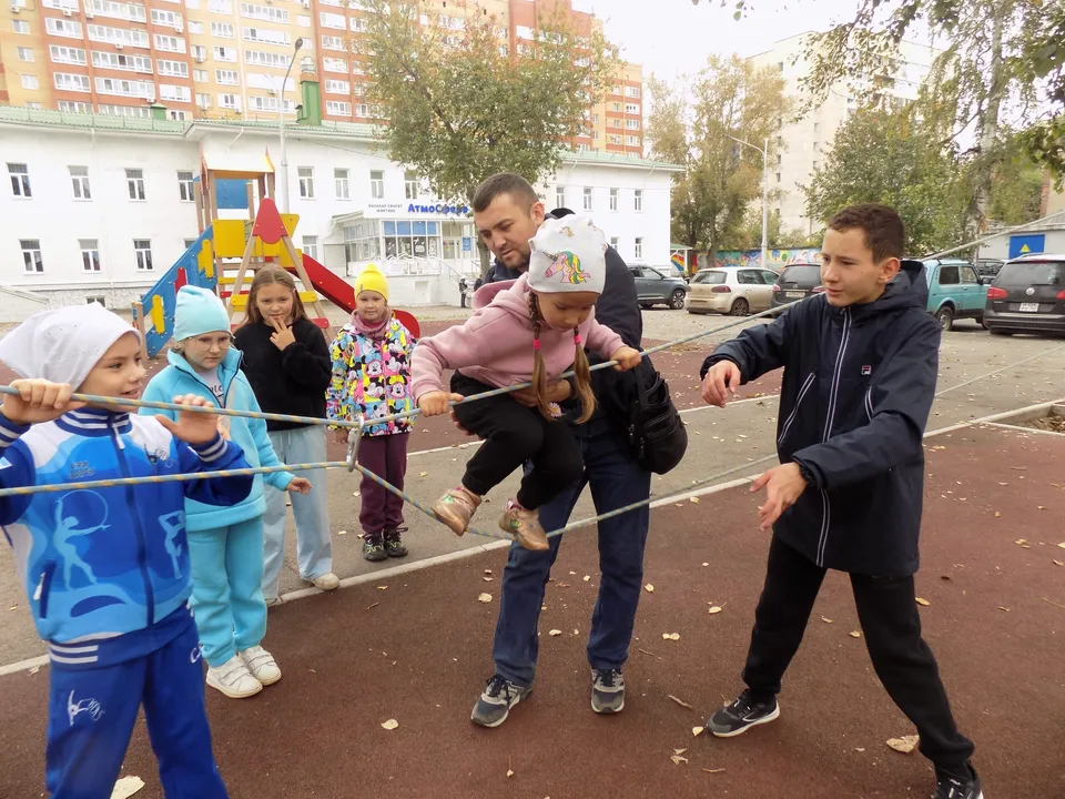 Дети играют в командную игру с верёвкой во дворе среди многоэтажек