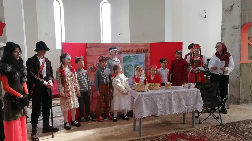 Дети в народных костюмах выступают на сцене с красным задником