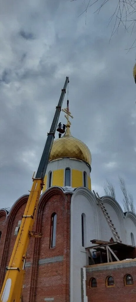 Кран поднимает золочёный купол с крестом на строящийся храм