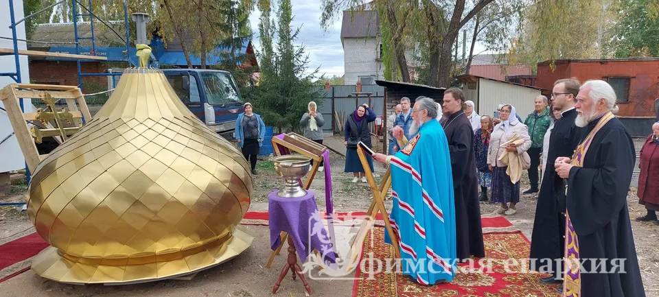 Митрополит Никон кропит святой водой золочёный купол, лежащий на земле у строящегося храма